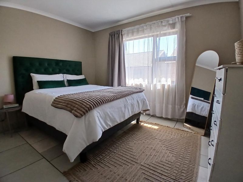 A well-maintained bedroom featuring neutral wall tones, tiled flooring, and a large window with installed curtain tracks for natural light.
