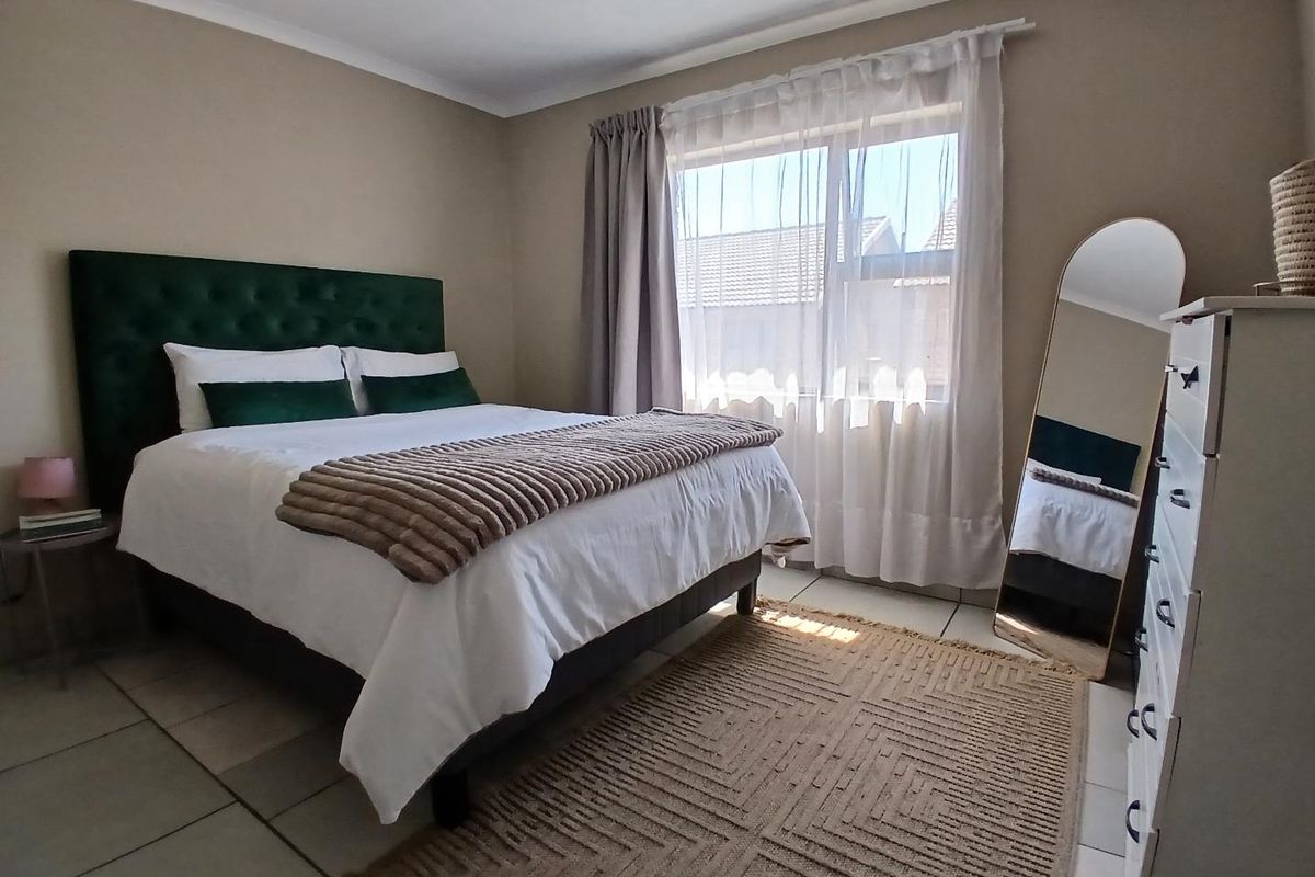 A well-maintained bedroom featuring neutral wall tones, tiled flooring, and a large window with installed curtain tracks for natural light.