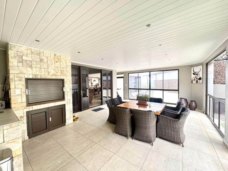 Spacious covered patio featuring a built-in braai with stone cladding, tiled flooring, and large aluminium sliding doors providing seamless indoor-outdoor flow.