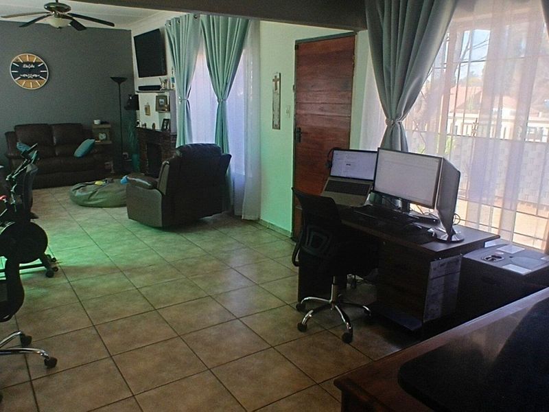 Spacious living area featuring tiled flooring, a ceiling fan, and large windows with security gates, offering a versatile layout for lounge and workspace configurations.