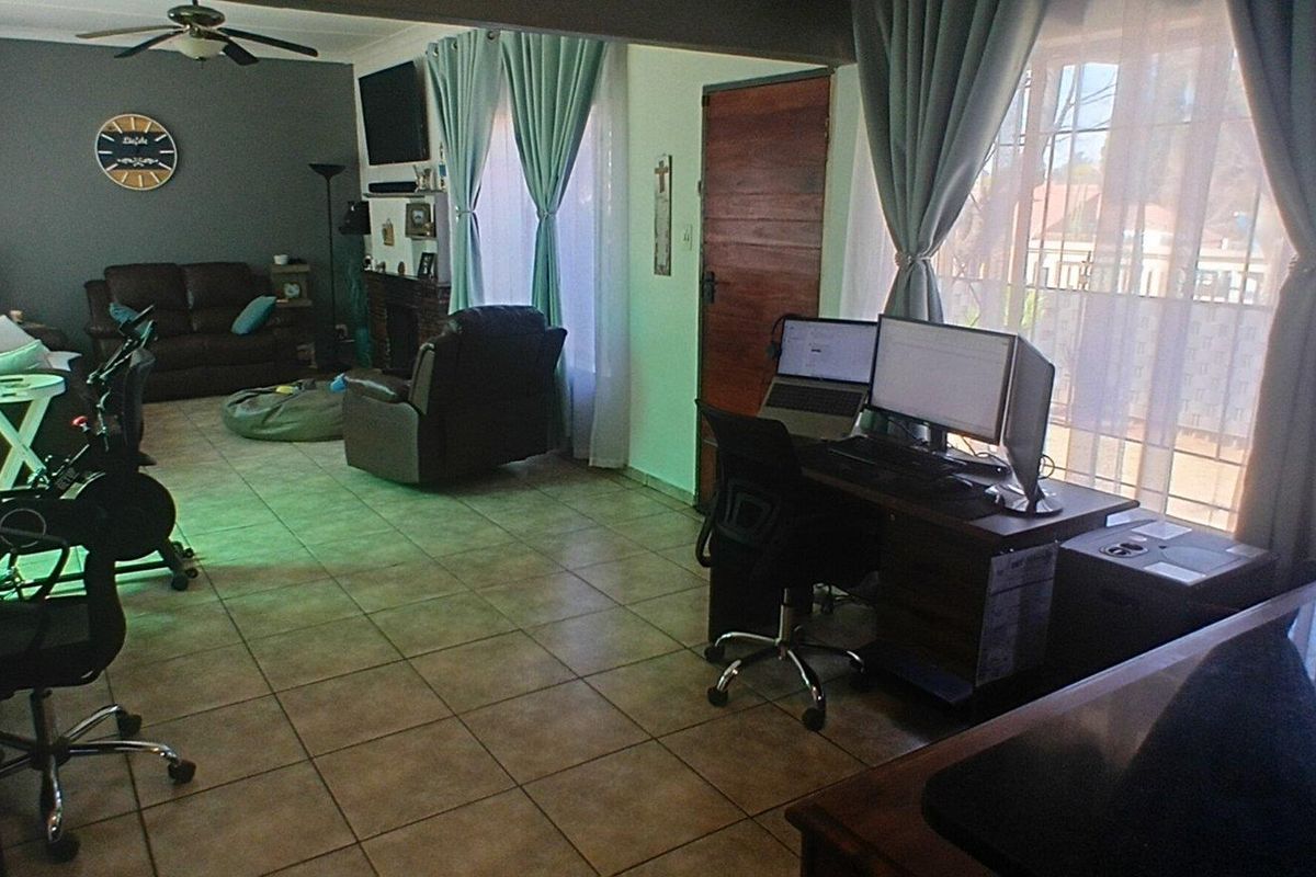 Spacious living area featuring tiled flooring, a ceiling fan, and large windows with security gates, offering a versatile layout for lounge and workspace configurations.