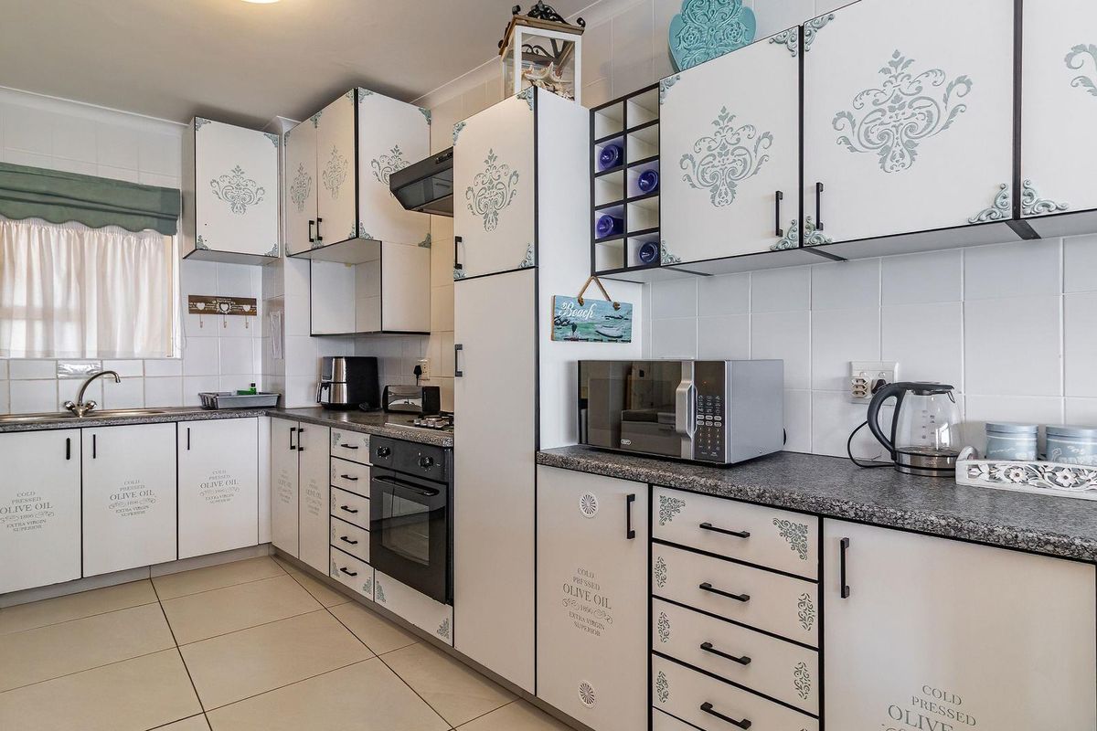 A functional kitchen featuring white cabinetry with decorative detailing, granite-look laminate countertops, built-in oven, extractor fan, and tiled finishes throughout.