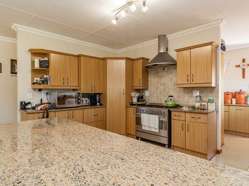 A functional kitchen featuring light wood cabinetry, granite countertops, a tiled backsplash, and a stainless steel gas stove with an extractor fan.