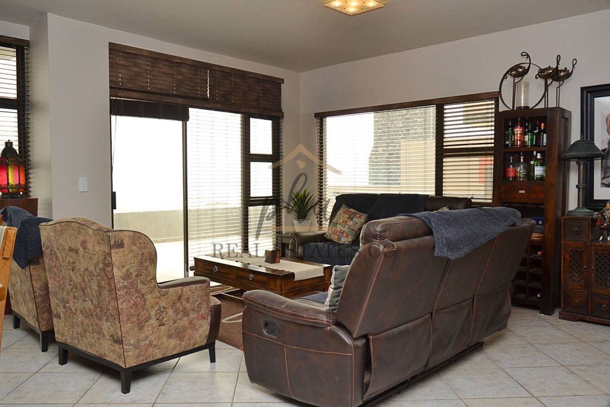 A comfortable living room featuring large windows with fitted blinds and sliding glass doors leading to an outdoor area.