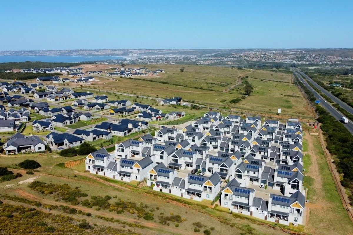 Aerial view of a modern residential estate featuring multiple detached homes with solar panels, situated in a coastal landscape near a major road.