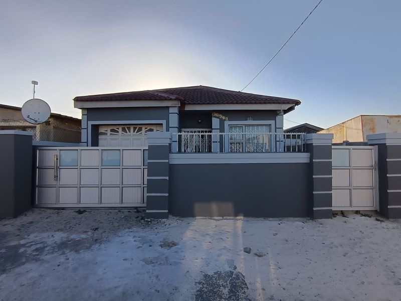 Front elevation of a single-story house featuring a tiled roof, secure perimeter wall with gates, and a garage.