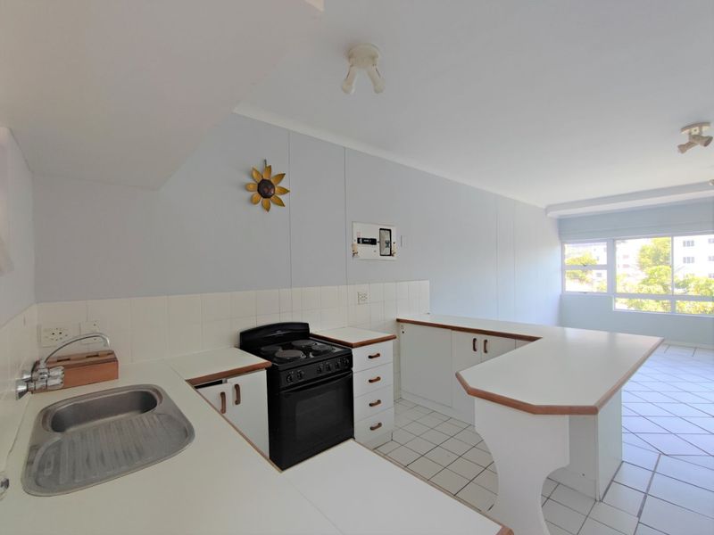 A functional, open-plan kitchen featuring white cabinetry, a freestanding stove, tiled backsplash, and a breakfast bar, offering a clean and bright workspace.