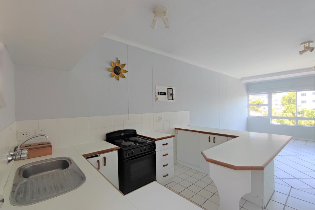 A functional, open-plan kitchen featuring white cabinetry, a freestanding stove, tiled backsplash, and a breakfast bar, offering a clean and bright workspace.