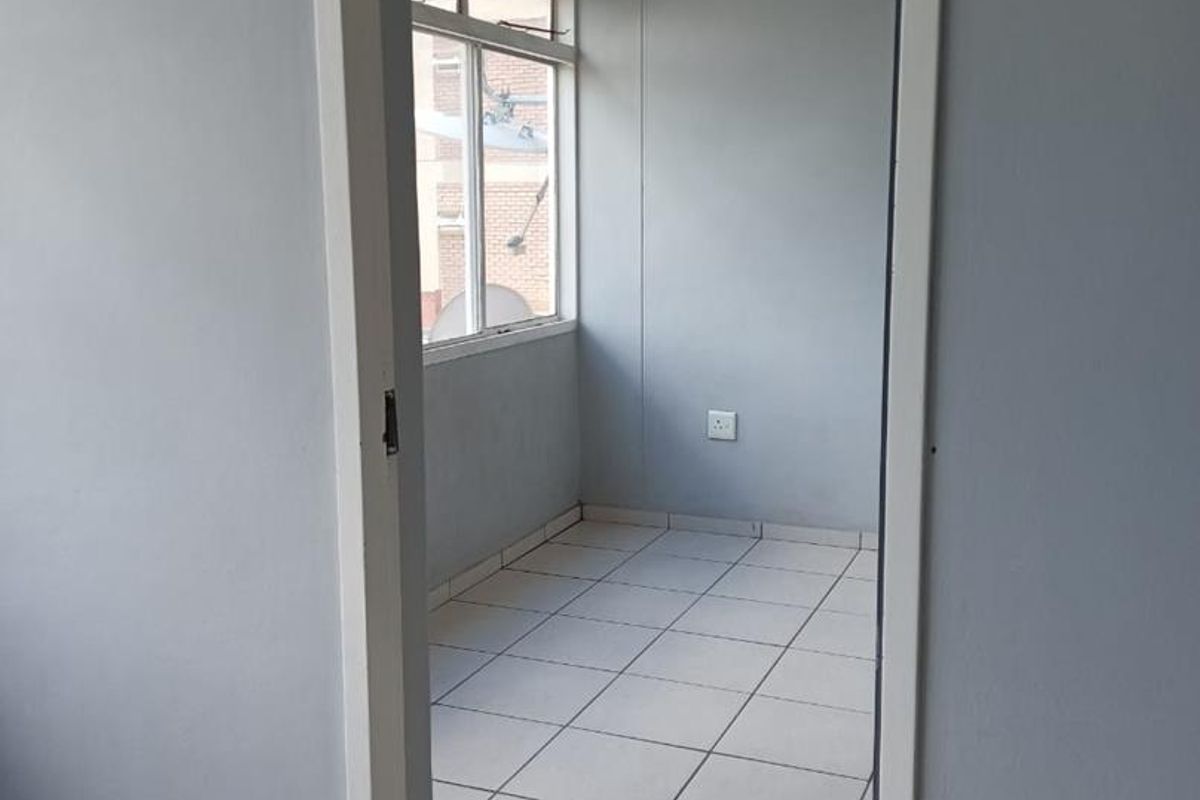 A compact, empty room featuring neutral grey walls, tiled flooring, and a window providing natural light, suitable for a home office or study.