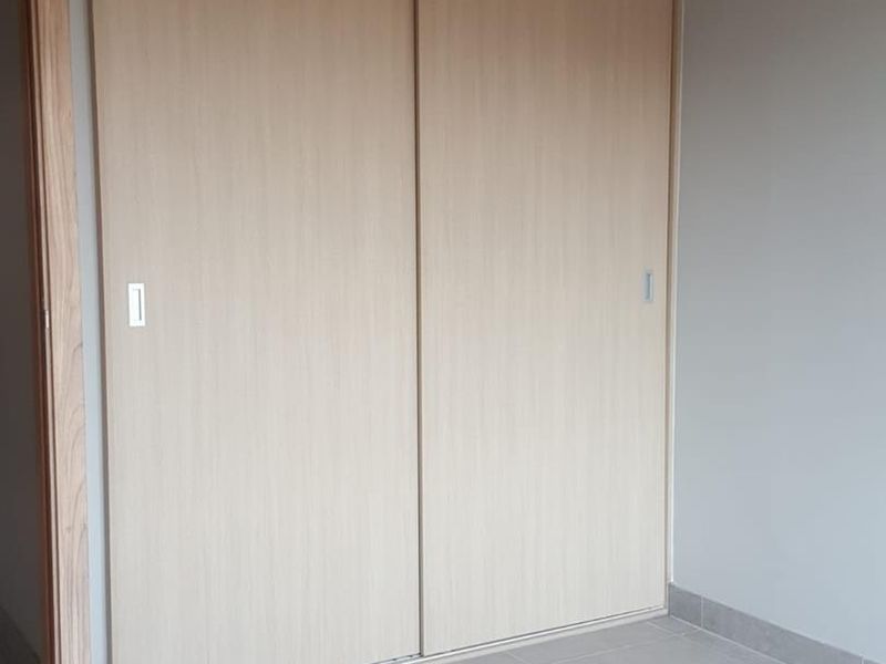 A clean, empty bedroom featuring modern light wood-finish built-in sliding door wardrobes and neutral grey floor tiles.