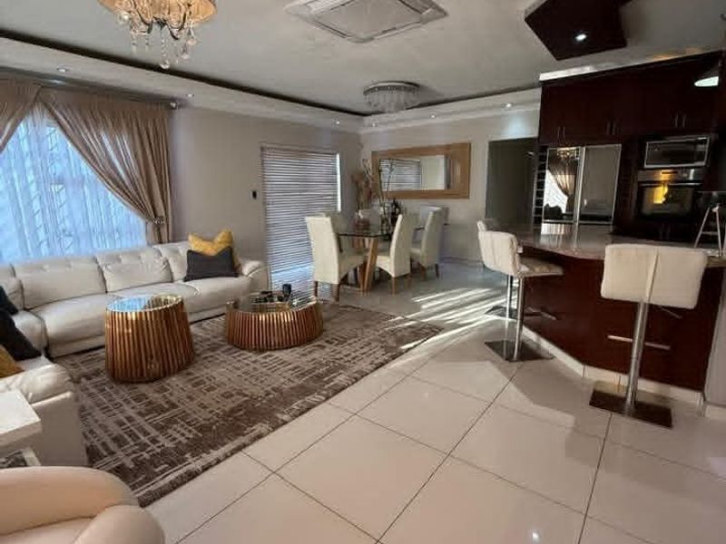 Spacious open-plan living, dining, and kitchen area featuring large porcelain floor tiles, modern cabinetry, and integrated appliances under a stylish coffered ceiling.