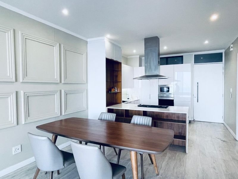 Modern open-plan living and kitchen area featuring a central island with built-in appliances, sleek cabinetry, and decorative wall paneling.