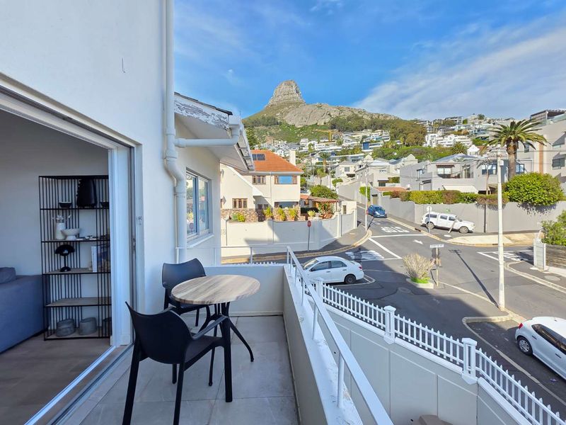 A balcony featuring tiled flooring and a protective railing, offering an elevated view of the surrounding neighborhood and mountain landscape.