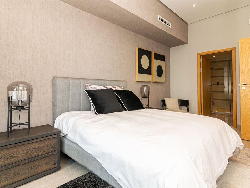 A modern, well-maintained bedroom featuring textured wallpaper, recessed ceiling lighting, ducted air conditioning, and direct access to an en-suite bathroom.