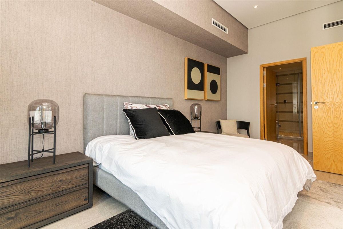 A modern, well-maintained bedroom featuring textured wallpaper, recessed ceiling lighting, ducted air conditioning, and direct access to an en-suite bathroom.