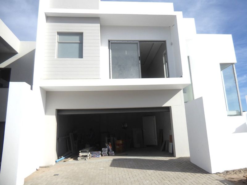 Modern two-story residential facade featuring a paved driveway, integrated garage, and clean white architectural lines.