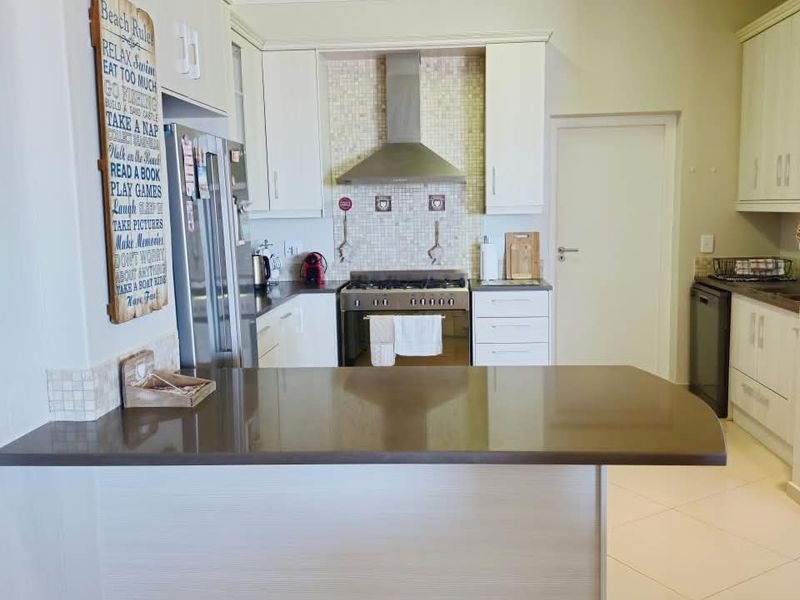 A well-maintained kitchen featuring stone countertops, a breakfast bar, stainless steel extractor fan, and built-in cabinetry with a tiled backsplash.