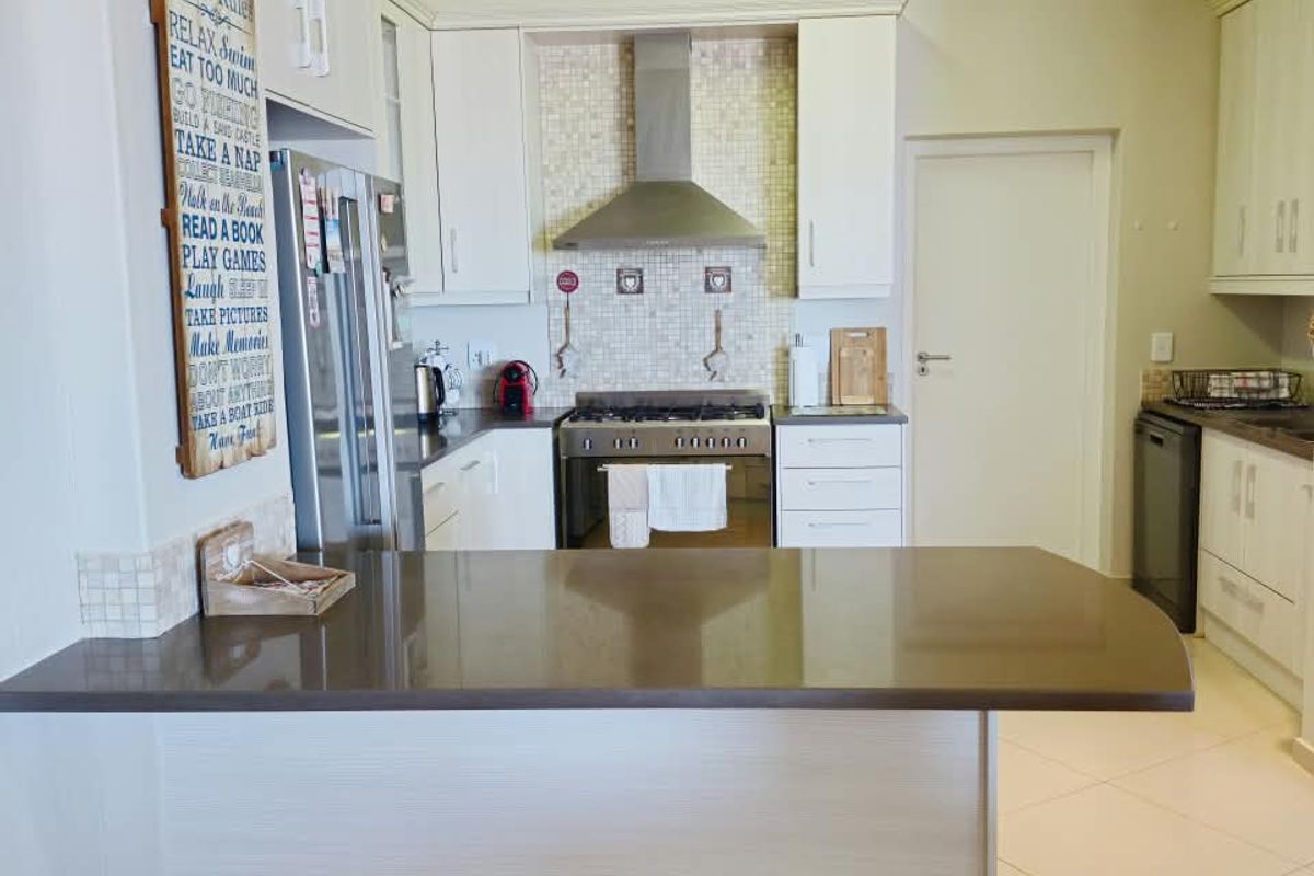 A well-maintained kitchen featuring stone countertops, a breakfast bar, stainless steel extractor fan, and built-in cabinetry with a tiled backsplash.