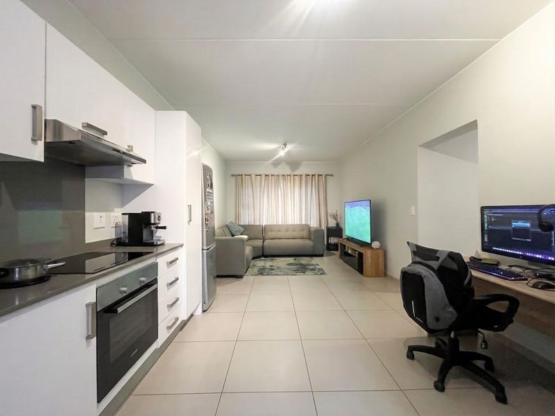 Modern open-plan living area featuring a sleek kitchen with built-in appliances, tiled flooring, and a dedicated built-in workspace.