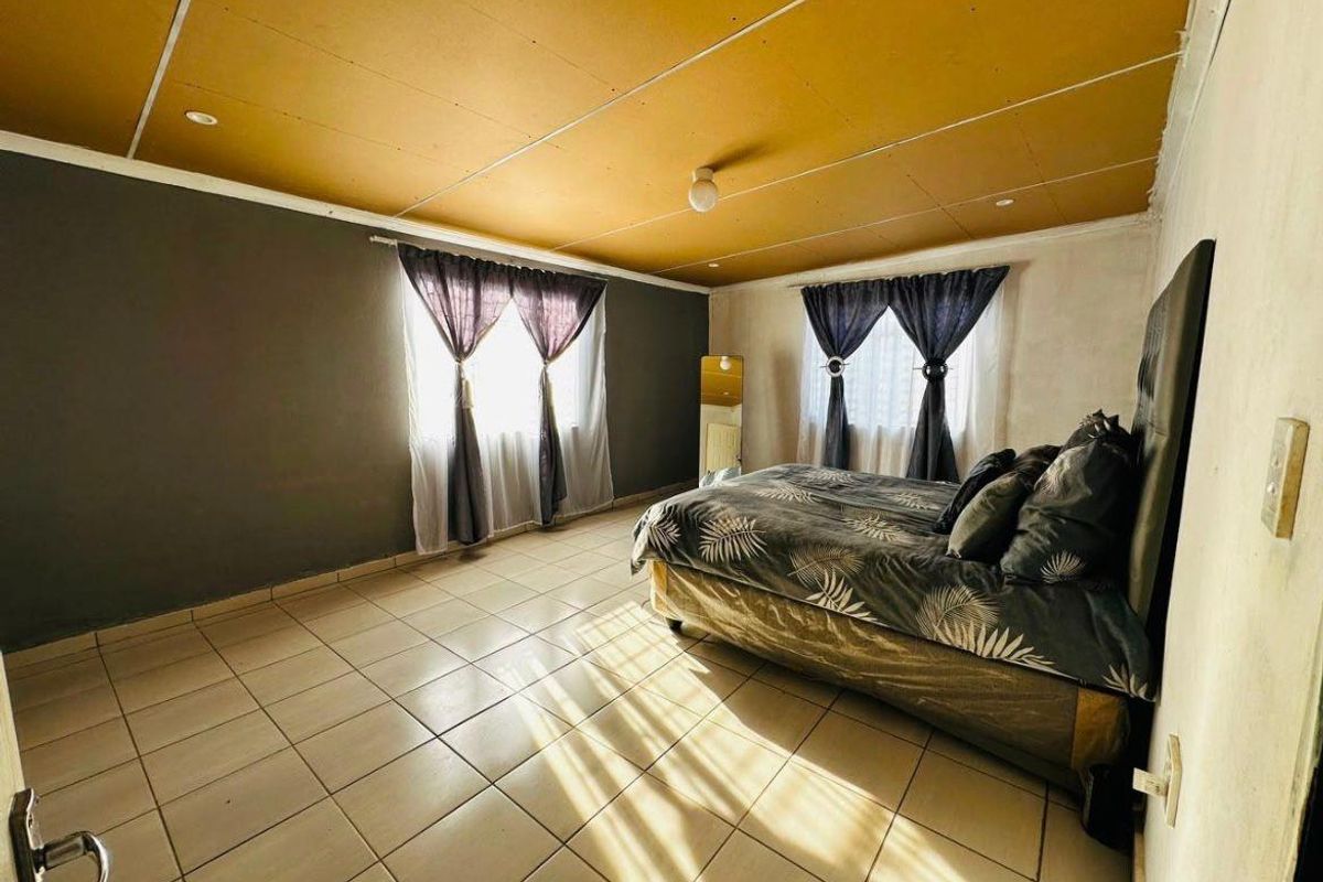 Spacious bedroom featuring tiled flooring, large windows with natural light, and a distinctive ceiling finish.