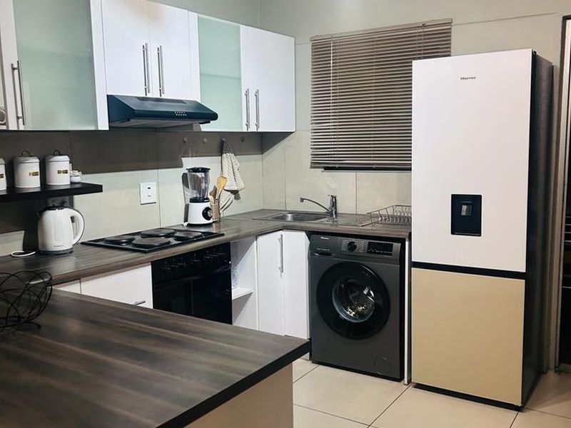 A functional kitchen featuring modern white cabinetry, dark laminate countertops, an integrated hob with extractor, and tiled flooring.