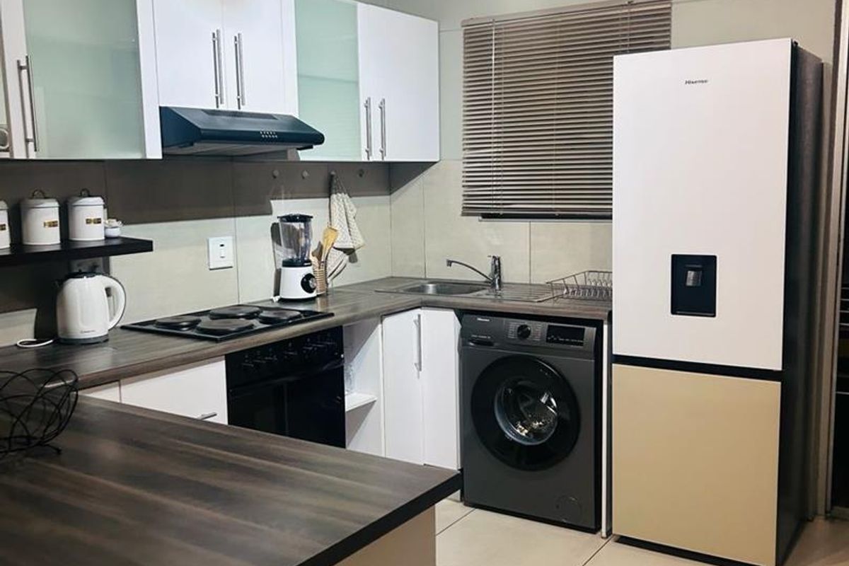 A functional kitchen featuring modern white cabinetry, dark laminate countertops, an integrated hob with extractor, and tiled flooring.