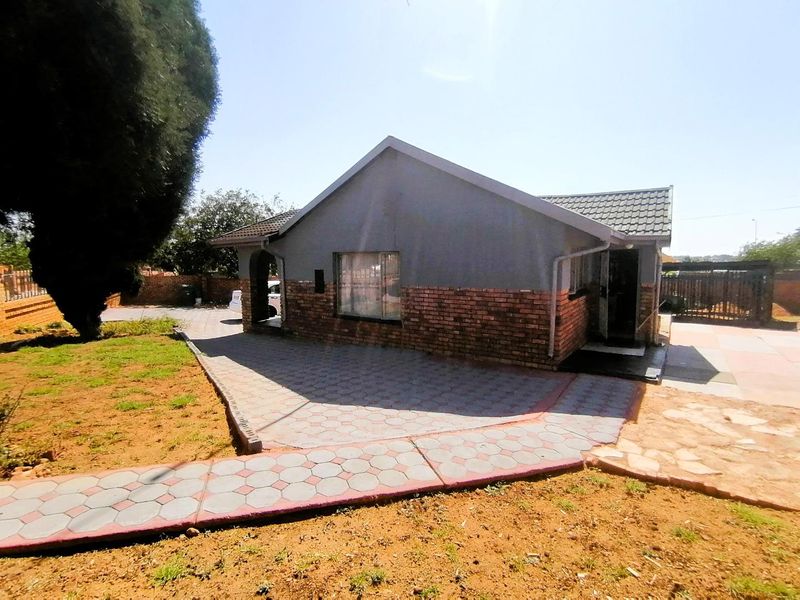 Front view of a single-story house featuring a brick and plaster facade, tiled roof, and paved driveway area.