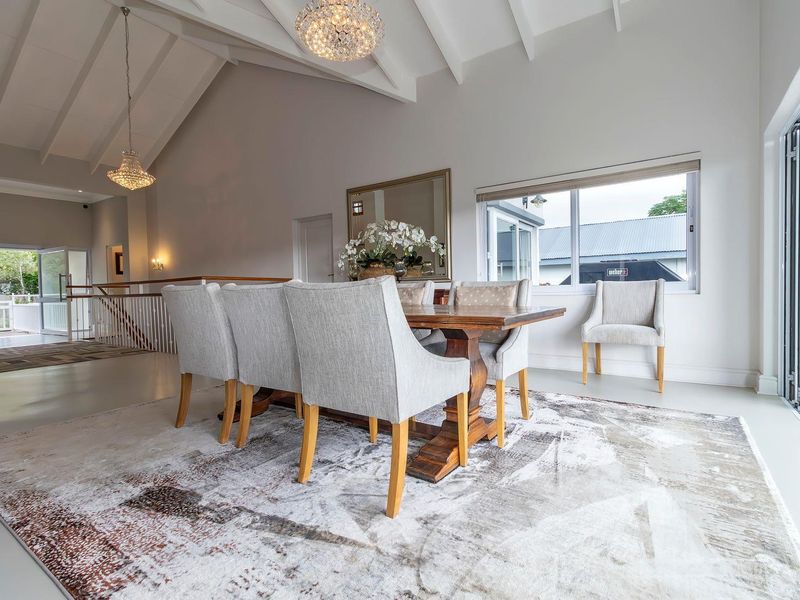 Spacious dining area featuring vaulted ceilings, exposed beams, elegant chandeliers, and large folding doors opening to an outdoor space.