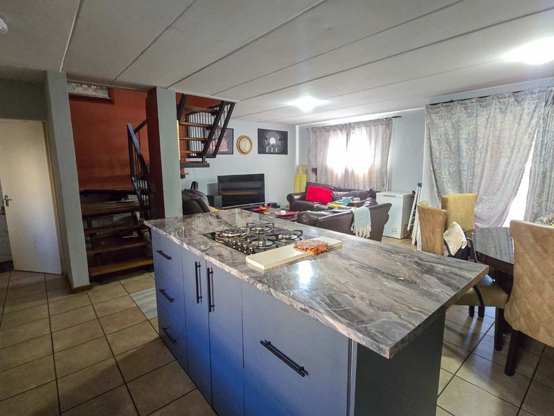 Open plan living area featuring a modern kitchen island with gas hob, tiled flooring, and an internal staircase leading to the upper level.