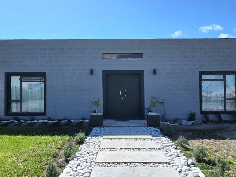 Front elevation of a modern concrete block house featuring a central double door entrance and a stone-paved walkway leading to the home.