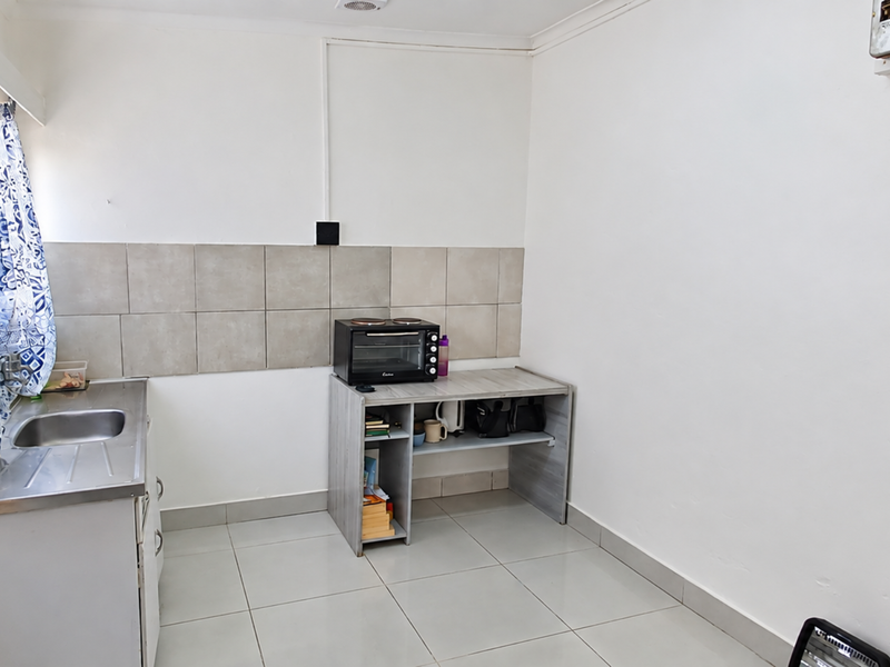 A compact kitchen area featuring a stainless steel sink, tiled backsplash, and tiled flooring with basic open shelving.