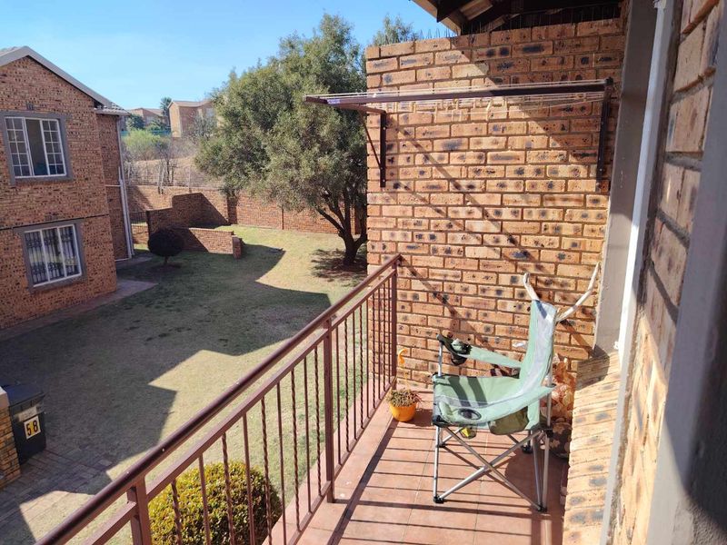 A private balcony featuring brick walls, metal railings, and tiled flooring, overlooking the complex garden area.