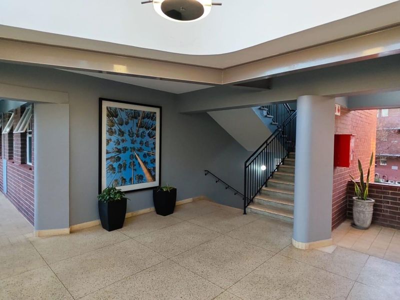 A well-maintained apartment building hallway featuring terrazzo flooring, a central staircase with metal railings, and recessed ceiling lighting.