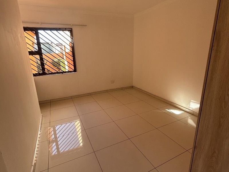 A clean, empty bedroom featuring neutral tiled flooring, a built-in cupboard, and a window fitted with security bars.