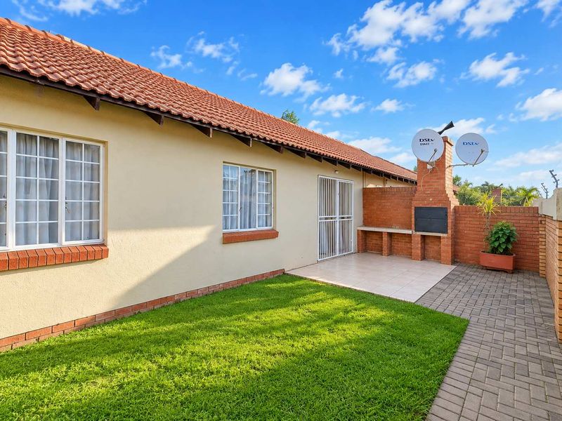 Rear exterior view of the townhouse featuring a private garden, paved patio area, and a built-in brick braai facility.