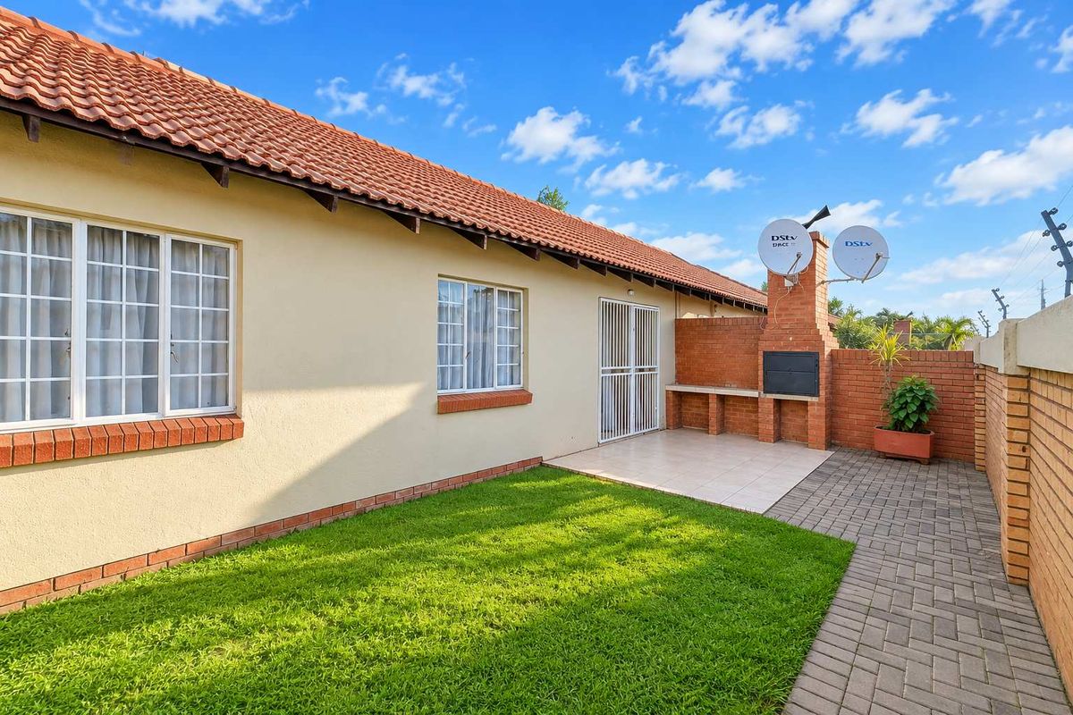 Rear exterior view of the townhouse featuring a private garden, paved patio area, and a built-in brick braai facility.
