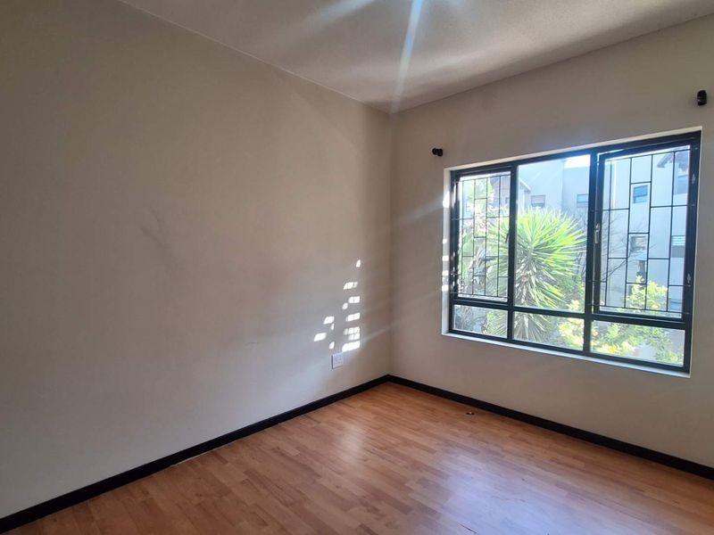An empty bedroom featuring laminate flooring, neutral walls, and a window fitted with security bars, offering a blank canvas for personalization.