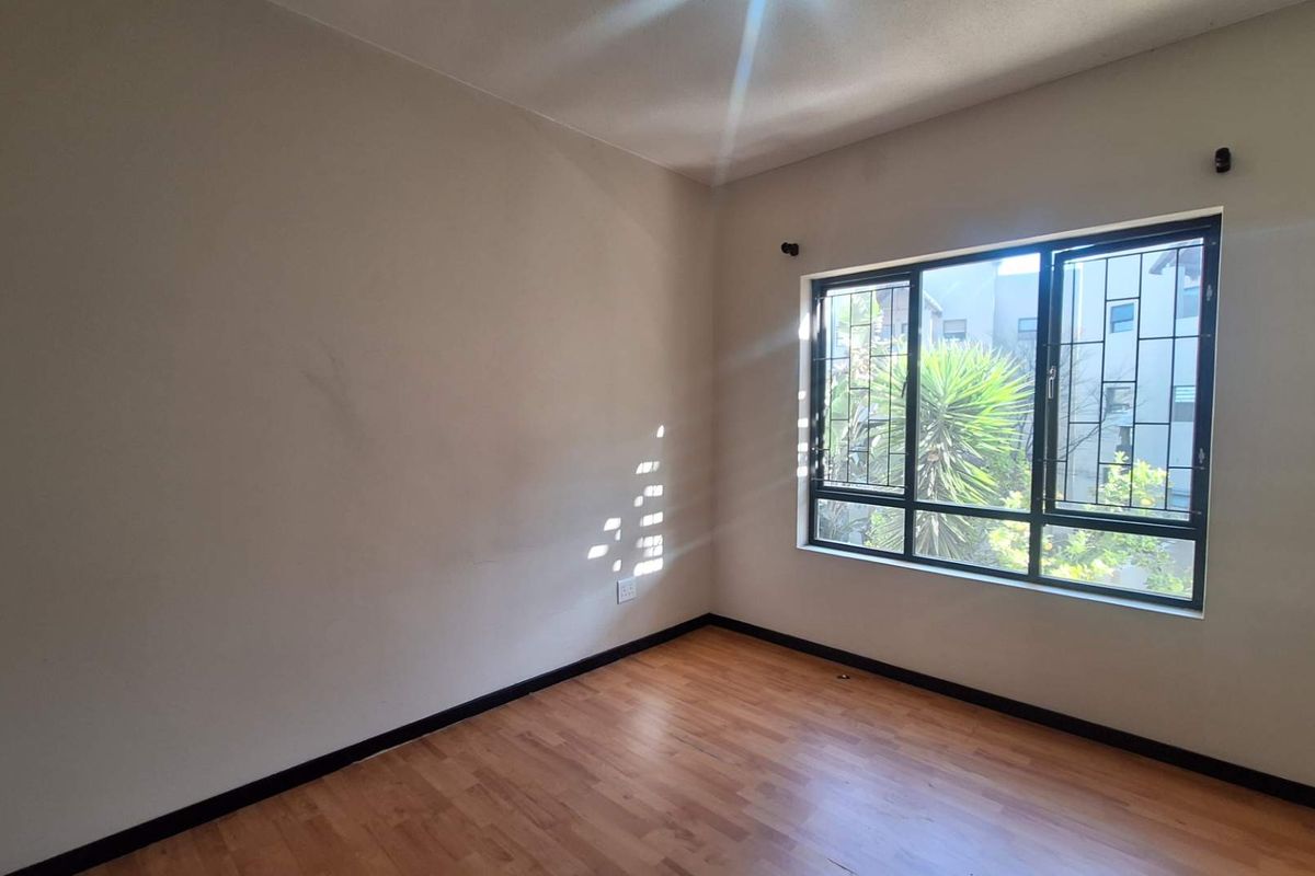 An empty bedroom featuring laminate flooring, neutral walls, and a window fitted with security bars, offering a blank canvas for personalization.
