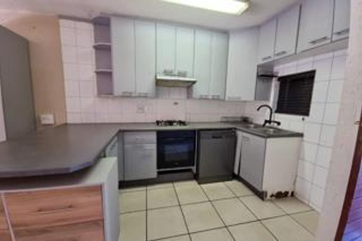 A functional kitchen featuring built-in cabinetry, a gas hob, oven, and tiled finishes, currently vacant and ready for cosmetic updates.