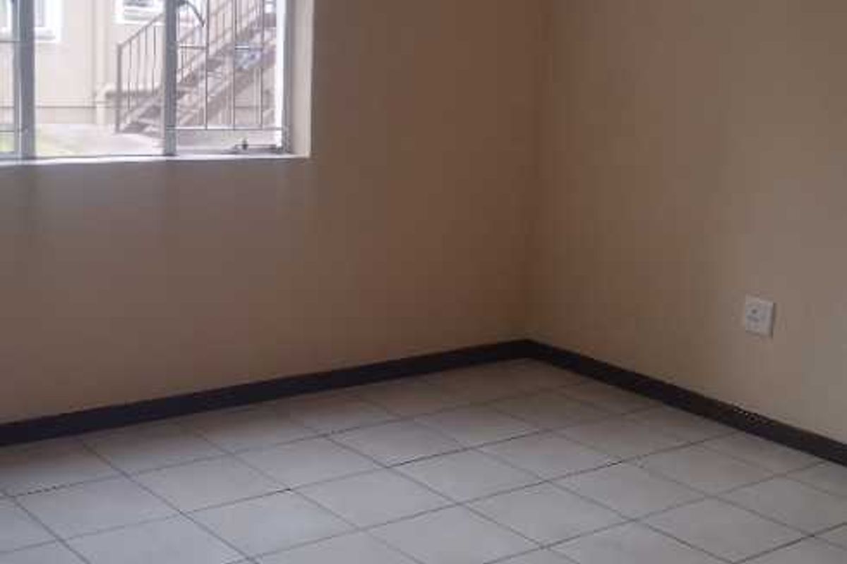 An empty bedroom featuring neutral wall paint, tiled flooring, and a window with security bars.