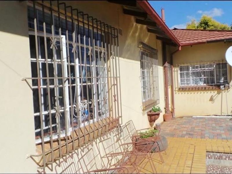 Rear exterior view of the house featuring a paved patio area, swimming pool, and security bars on the windows.