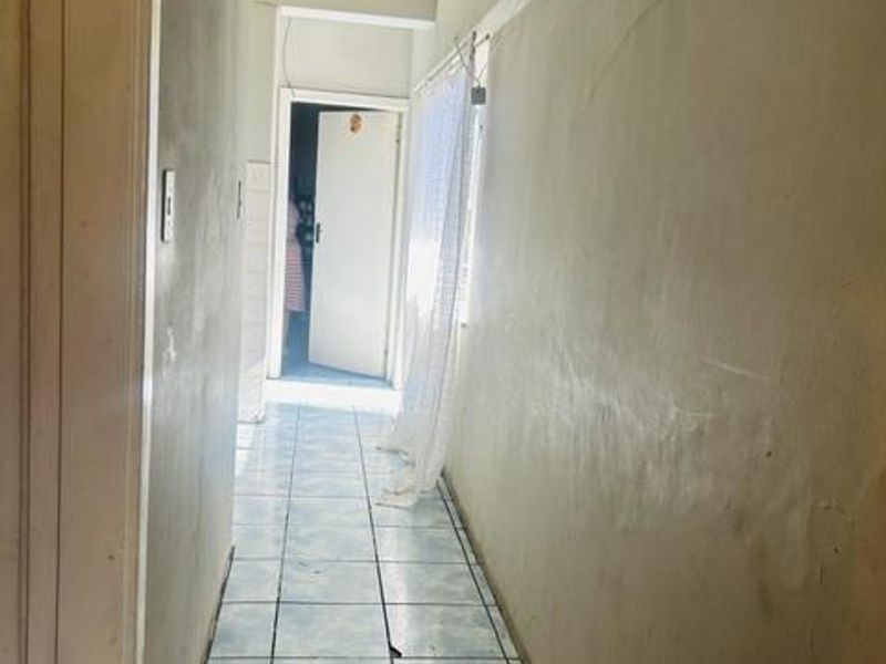 A narrow hallway featuring tiled flooring and plain walls, leading to an internal doorway.
