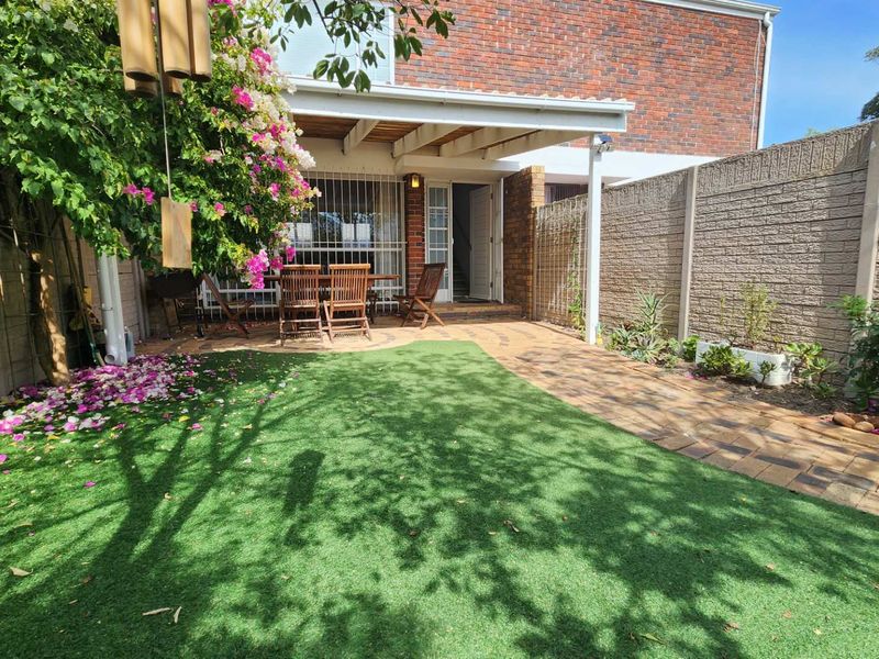 A private rear courtyard featuring a covered patio, paved pathways, and a low-maintenance artificial lawn enclosed by brick boundary walls.