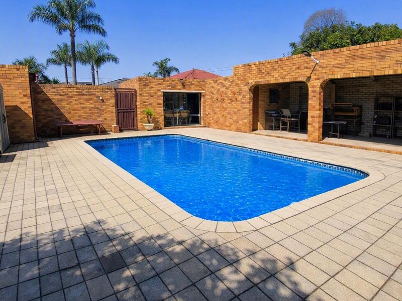 Outdoor pool area featuring a paved deck, a covered patio space, and enclosed by a brick boundary wall.