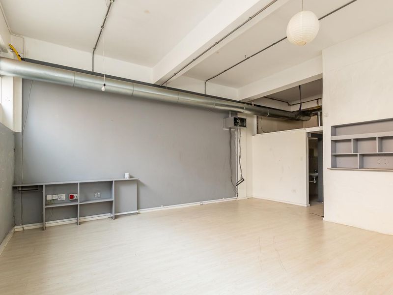 An open-plan industrial style space featuring exposed ductwork, laminate flooring, and built-in shelving, suitable for a studio or office environment.