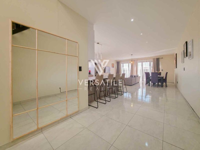 Spacious open-plan living and dining area featuring polished tiled flooring, recessed downlighting, and a large decorative wall mirror.