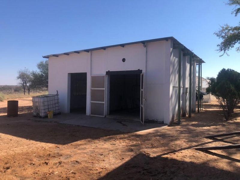 A detached utility building or workshop on a farm property, featuring a concrete base and metal-framed access doors.