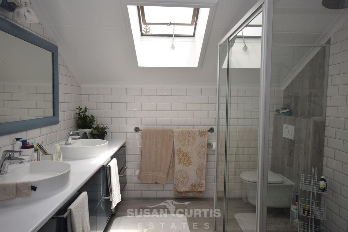 Modern bathroom featuring a double vanity with vessel sinks, a glass-enclosed shower, and a skylight providing natural light.