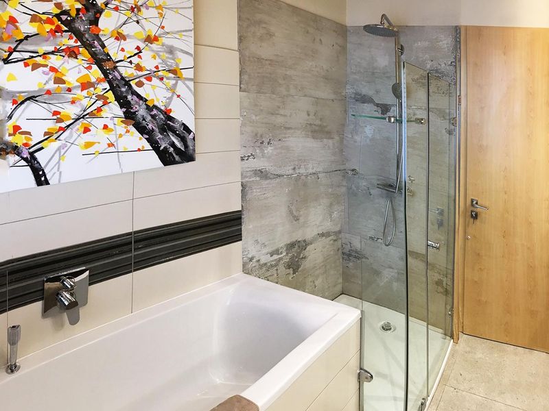 Modern bathroom featuring a built-in bathtub, a separate glass-enclosed shower with contemporary wall tiling, and high-quality fixtures.