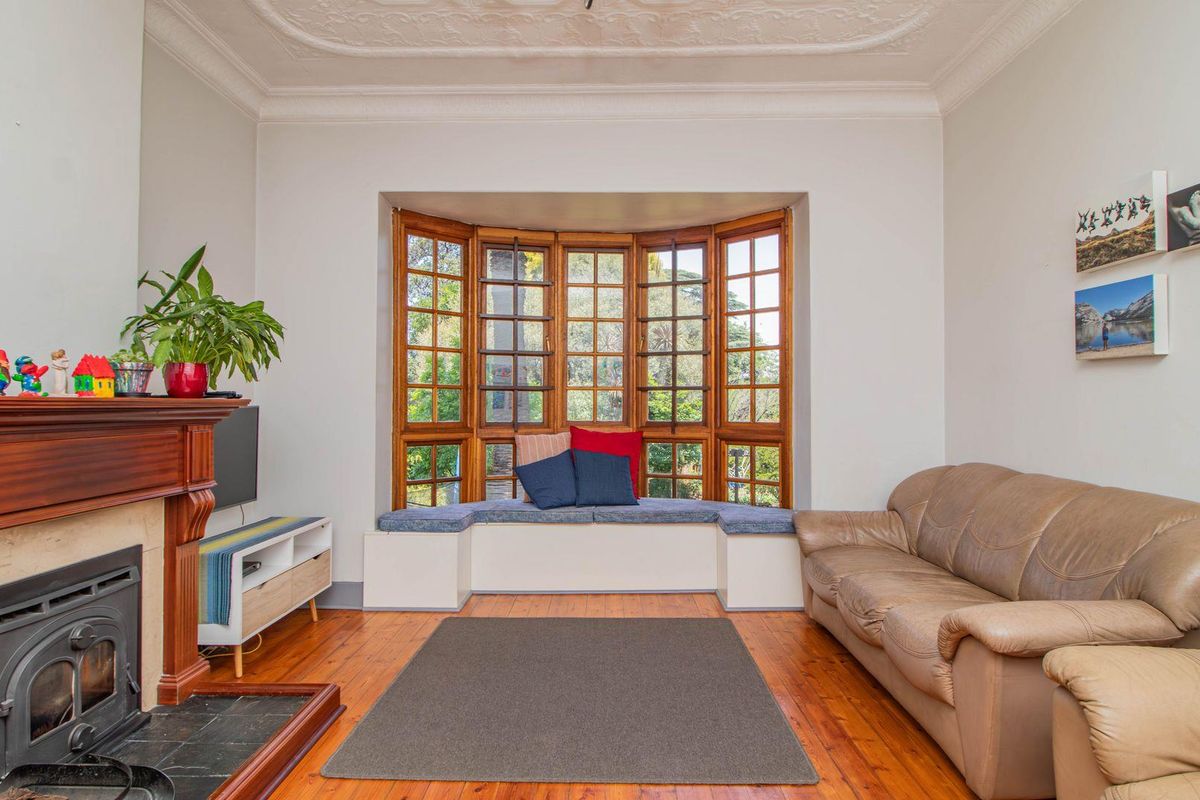 A cozy living room featuring a classic fireplace with a wooden mantel, polished timber flooring, and a charming bay window with built-in seating.
